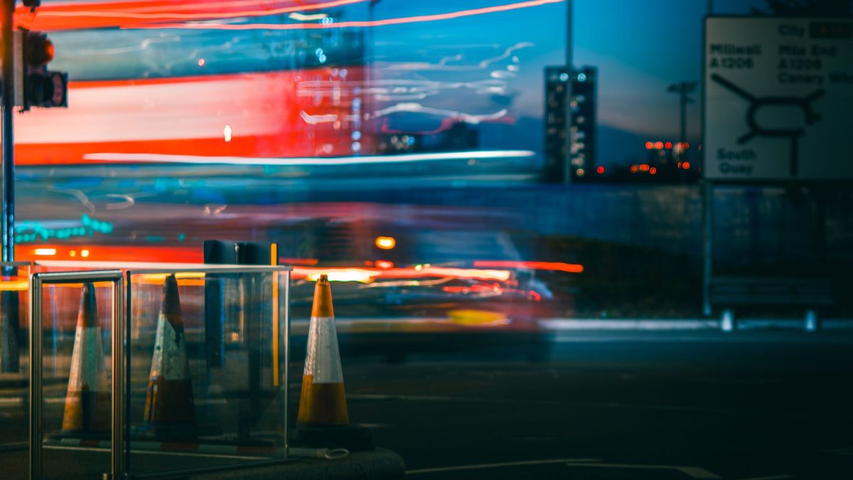 Orange traffic cones on a city street at night with blurred light trails