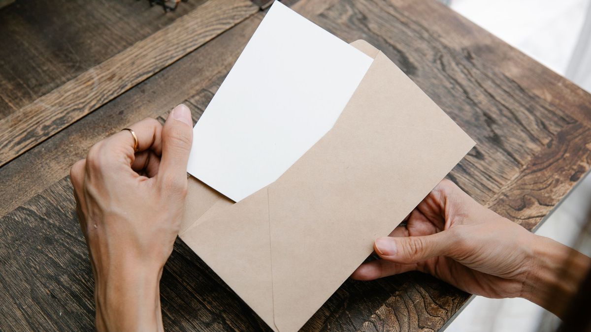 Hands sliding a blank sheet of paper out of a brown envelope on a wooden table
